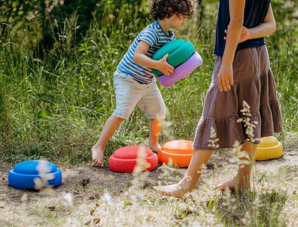 Boy and girl setting up an outdoor stepping stones obstacle course with Stapelstein