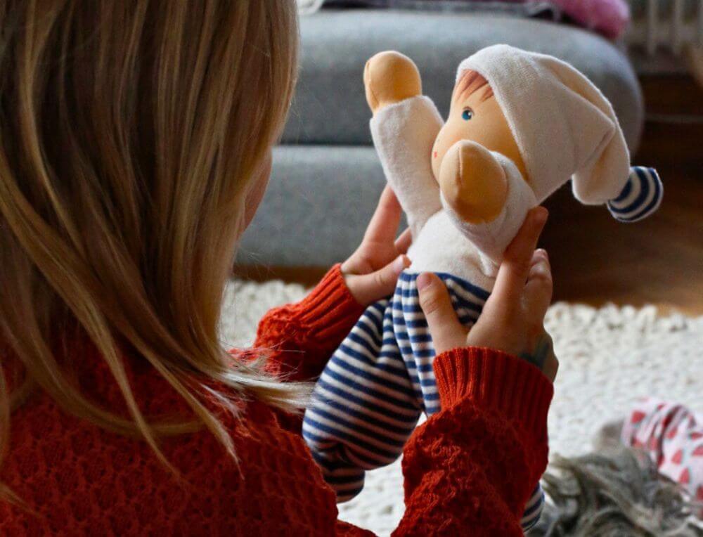 Child playing with a Nanchen Natur doll on a warm woolen rug